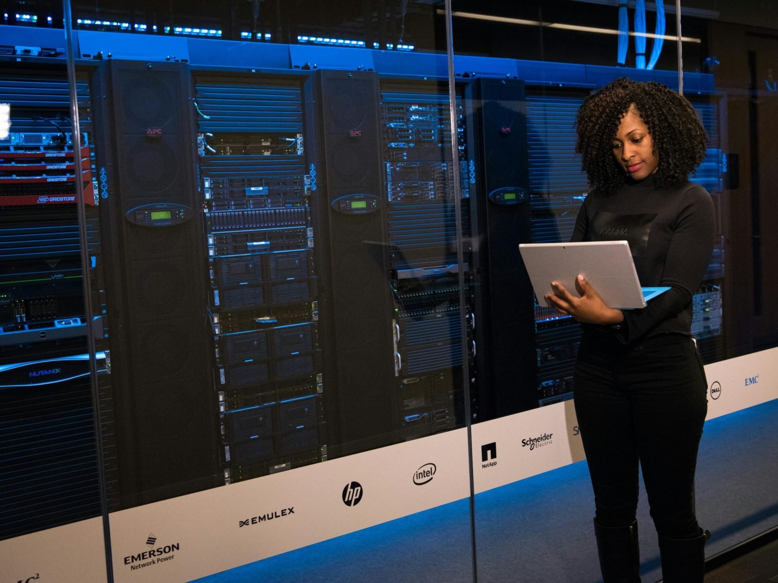 A female engineer using a laptop while monitoring data servers in a modern server room.